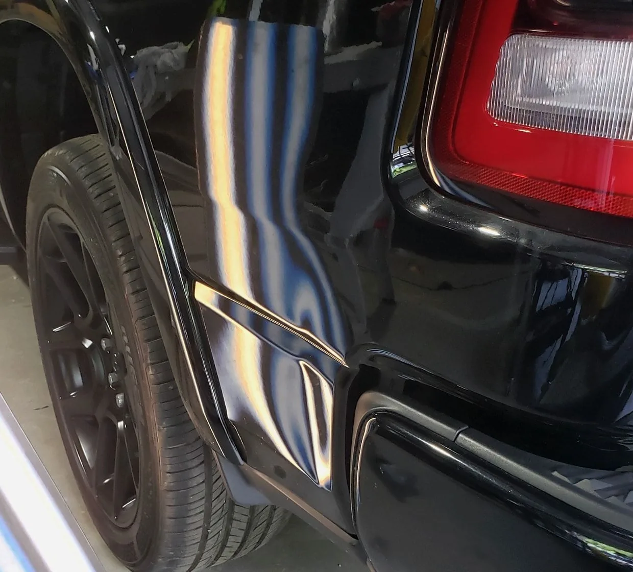 A black quarter panel with a long crease picked out by a reflected light board