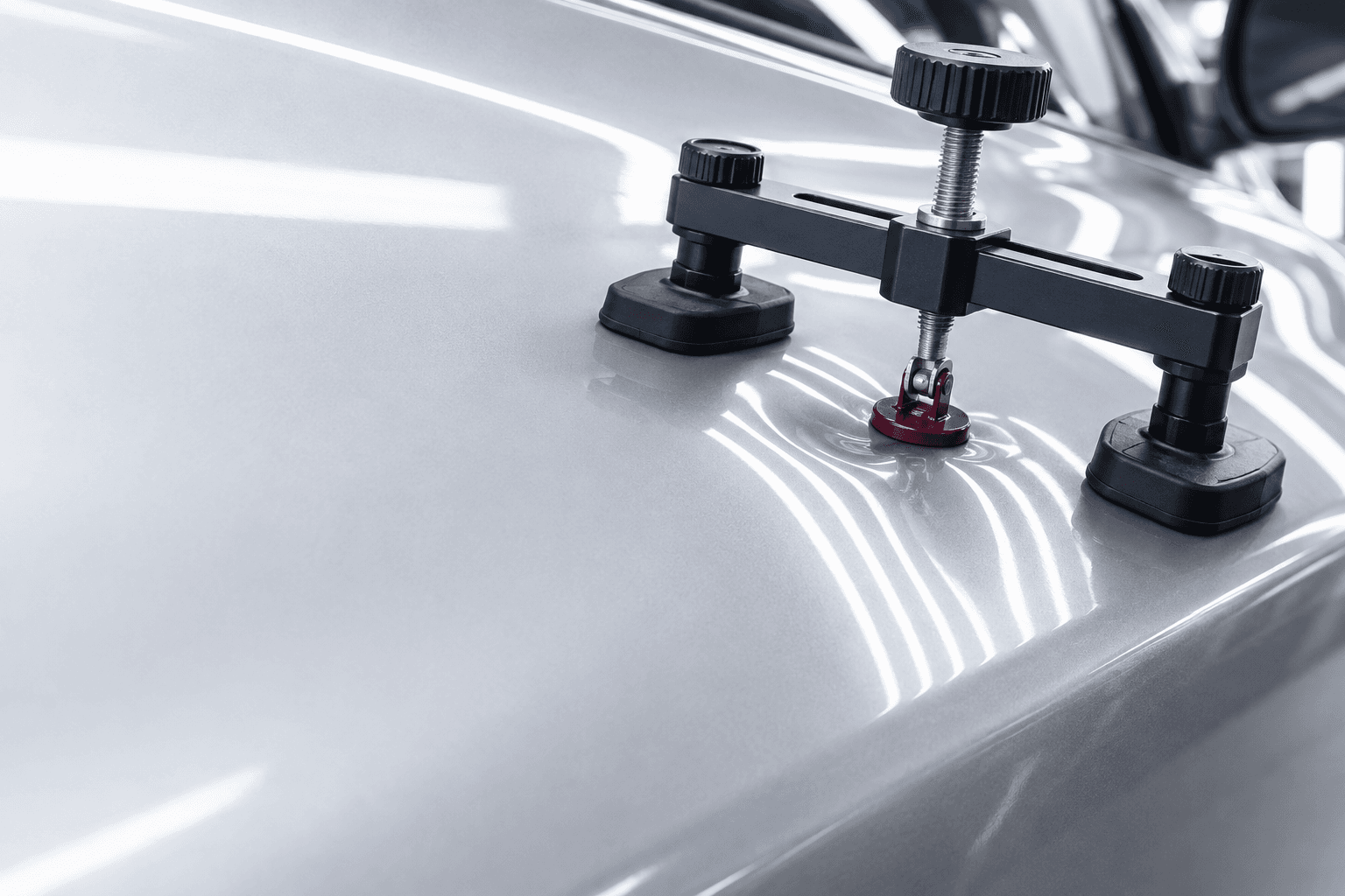 Paintless dent repair bridge puller positioned on a silver panel under inspection lights